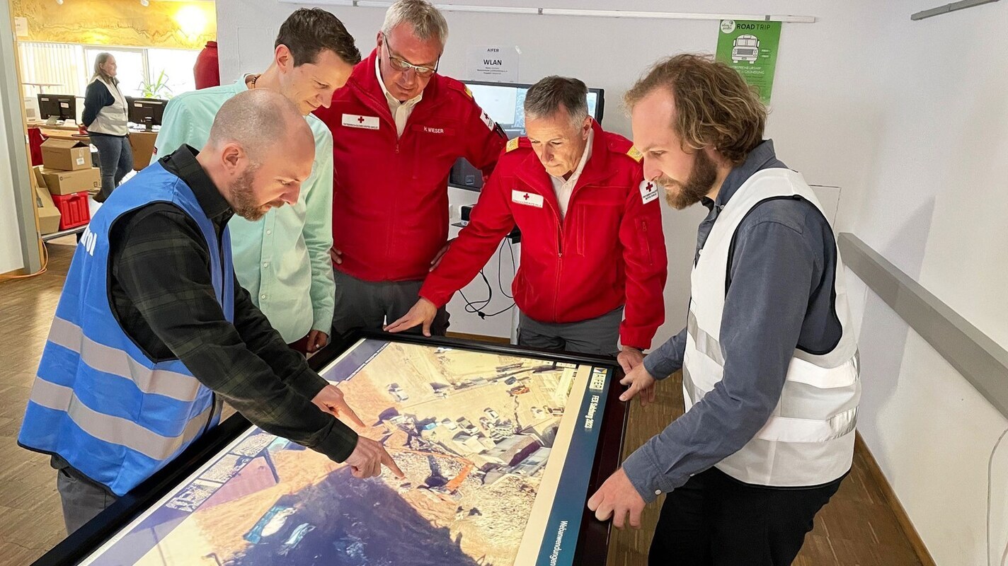 Dr. Marc Wieland (links) vom Earth Oberservation Center im DLR bespricht sich mit anderen Beteiligten der Katastrophenschutzübung in Salzburg. Das DLR war im Rahmen des Projekts AIFER vor Ort. In dem Projekt arbeiten die Forschenden mit Methoden der Künstlichen Intelligenz, um Informationen aus der Erdbeobachtung und aus dem Internet zu kombinieren. Bild: Rotes Kreuz Salzburg